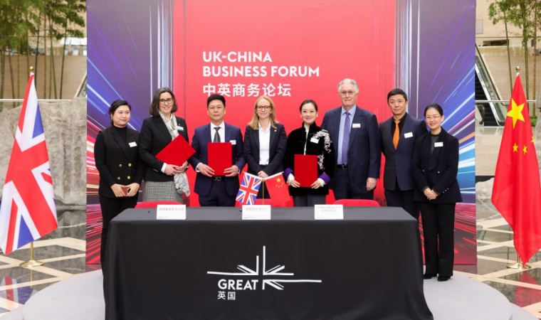 Group of eight professionals standing behind a signing table at a UK–China Business Forum, with UK and China flags on the table and a bold red backdrop.