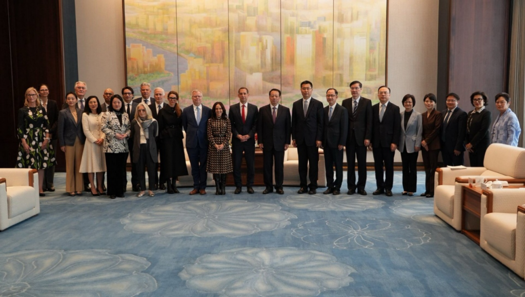 Group of business professionals posing for a formal photo in a modern lobby with a large mural behind them.